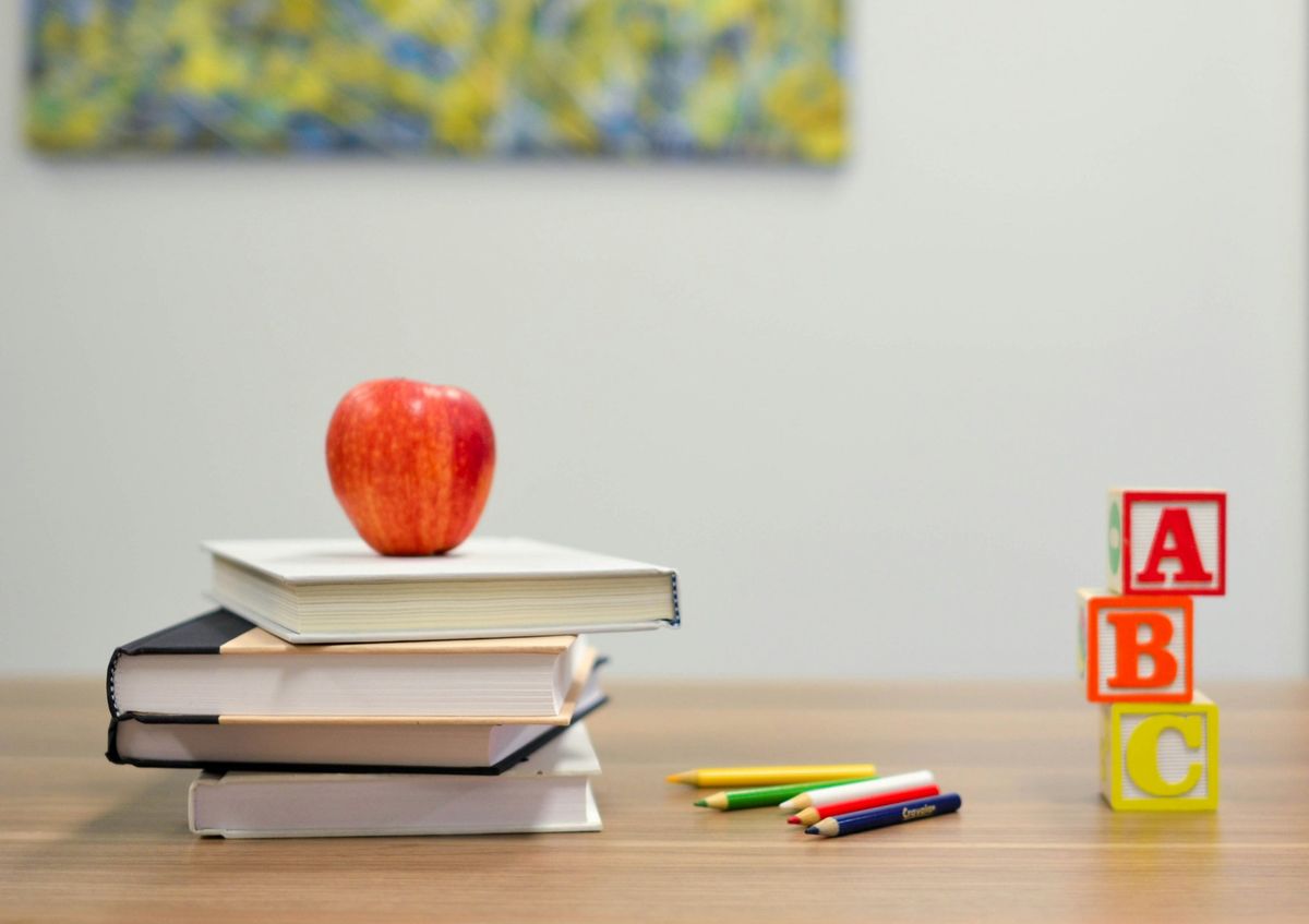Books, an apple, coloured pencils and ABC blocks on a desk